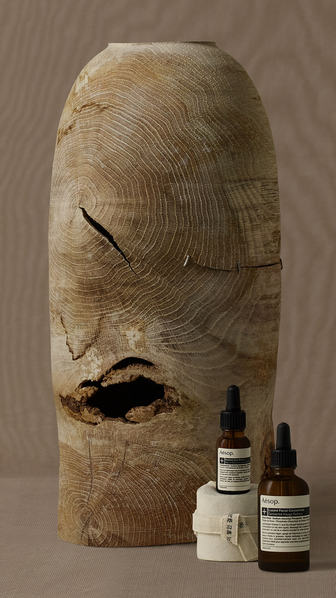Lucent Facial Concentrate and Exalted Eye Serum with Bojagi wrapping cloth ahead of a wooden art piece