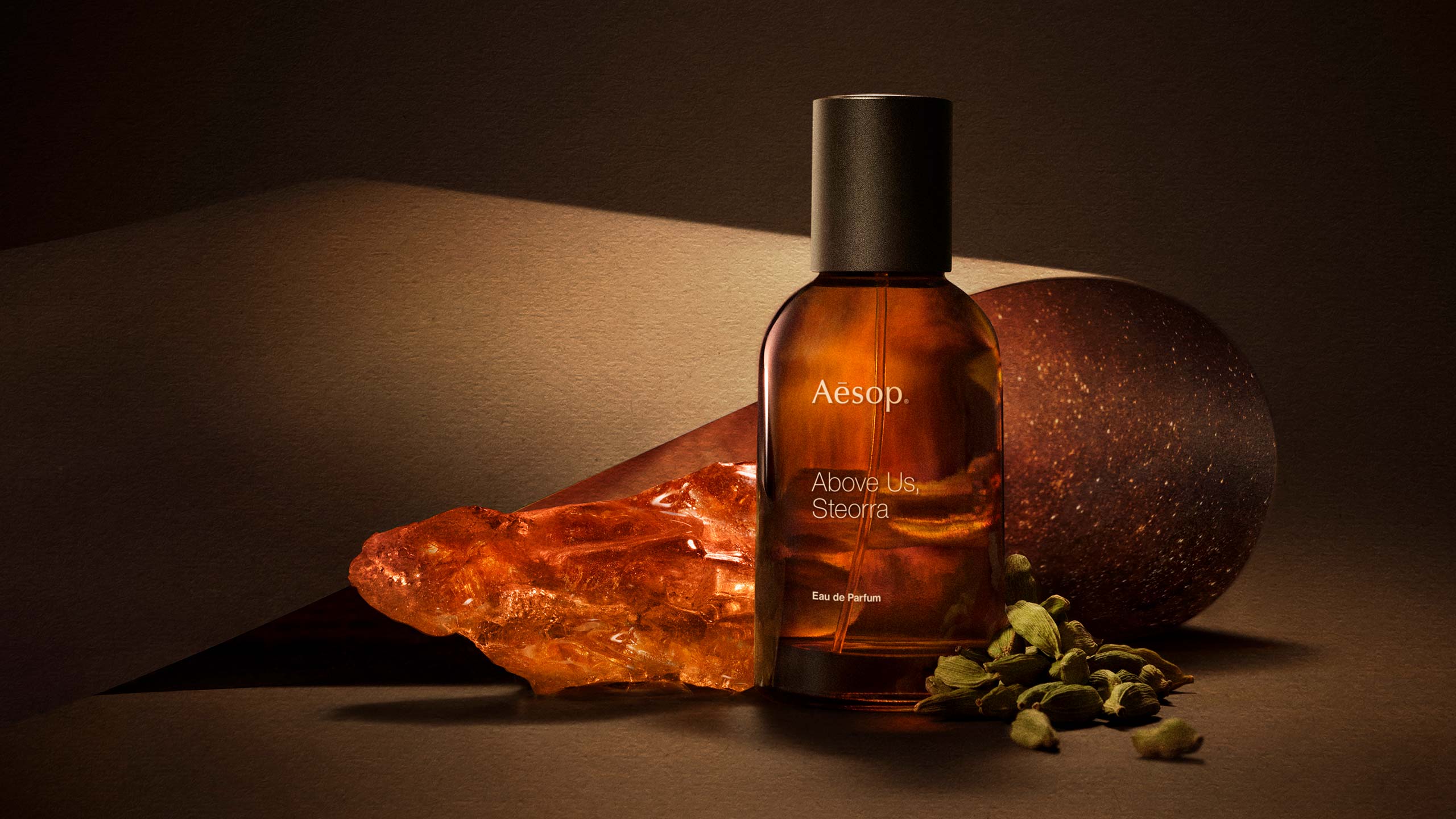 A bottle of above of steorra EDP, amber and cardamom placed in brown background lit up with warm lighting