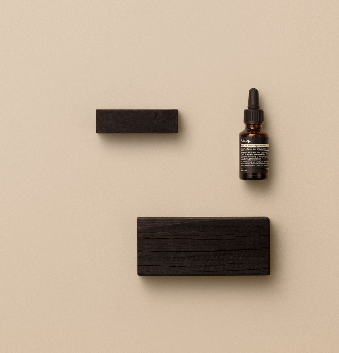 Aesop Sage & Cedar Scalp Treatment placed next to wooden blocks in a beige surface